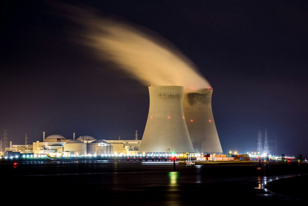 Two nuclear power plant cooling towers releasing steam at night beside a river