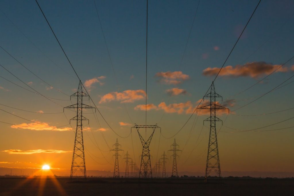 High-voltage transmission towers silhouetted against a sunset sky