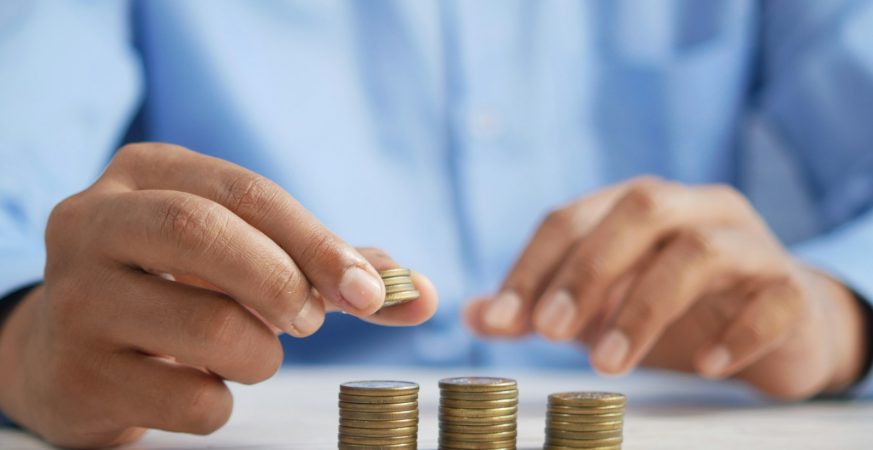 A hand stacking coins into growing piles on a table