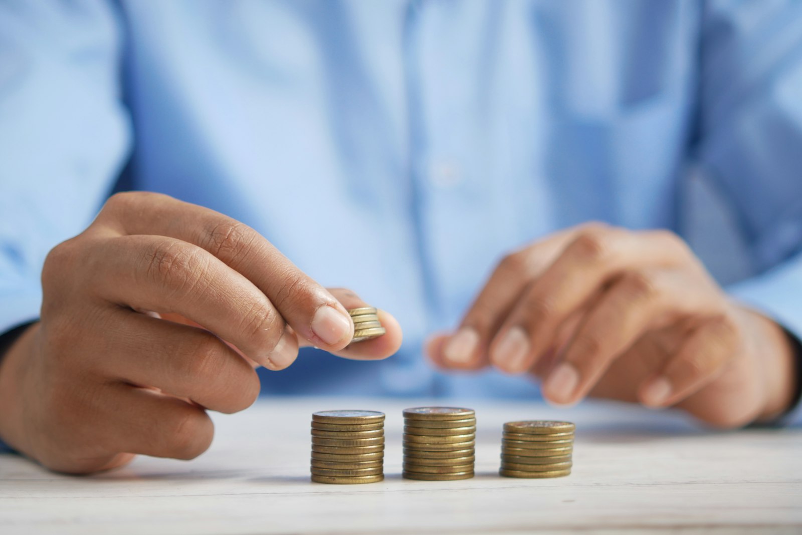 A hand stacking coins into growing piles on a table