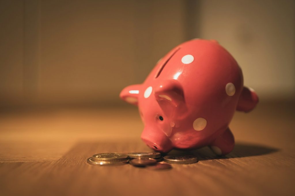A coin being dropped into a pink piggy bank on a wooden table