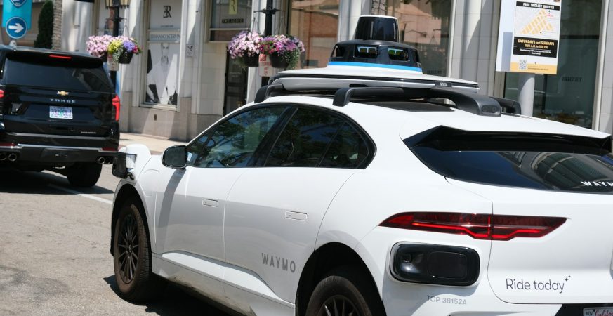 A white Waymo autonomous vehicle with roof-mounted sensors parked on a Los Angeles street