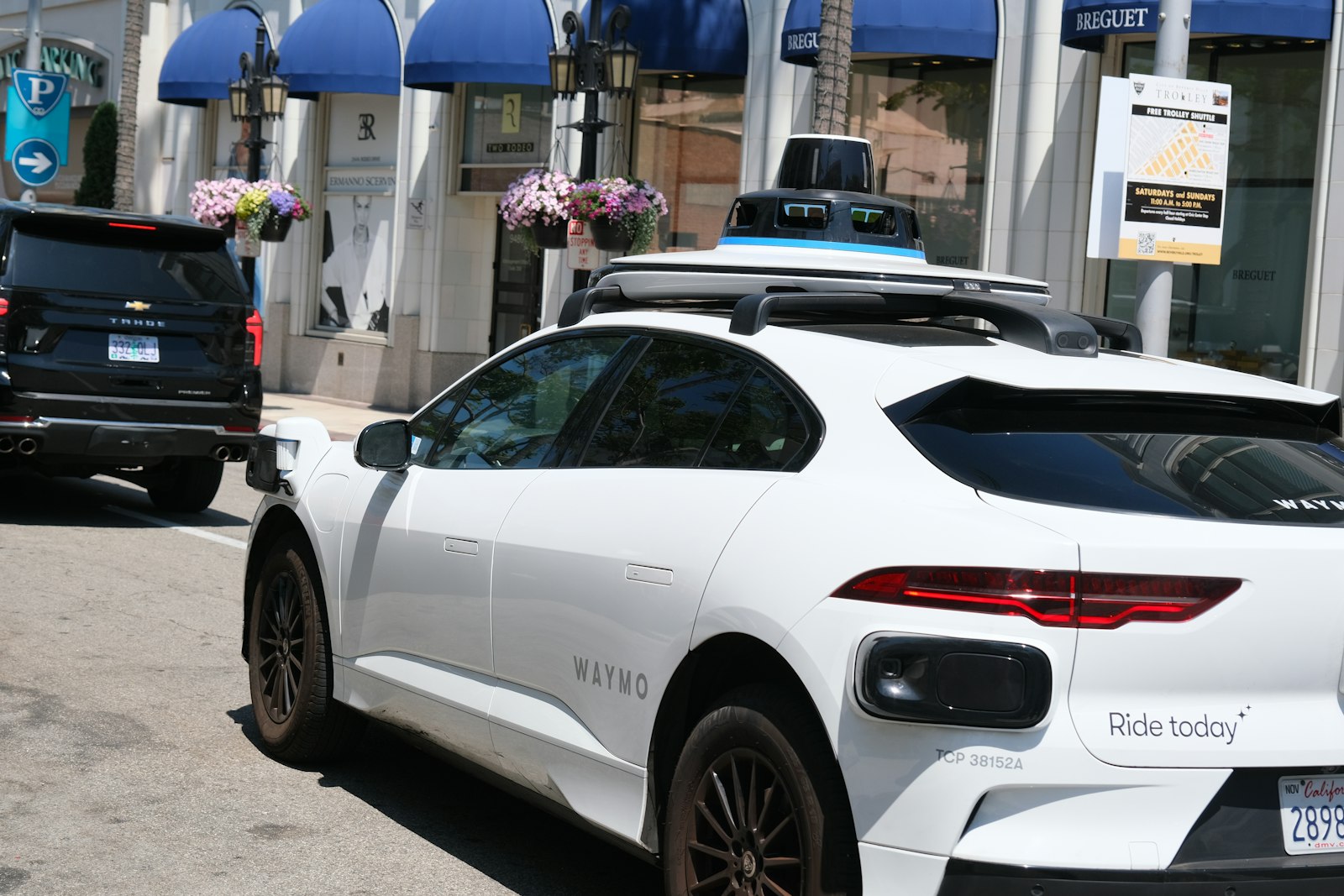 A white Waymo autonomous vehicle with roof-mounted sensors parked on a Los Angeles street