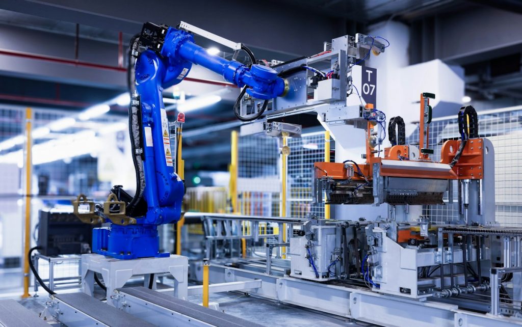 A blue industrial robot arm moving a refrigerator panel on a factory line