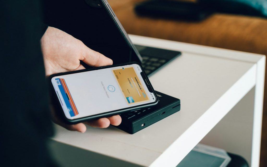 A hand holding a smartphone over a card reader to make a contactless payment