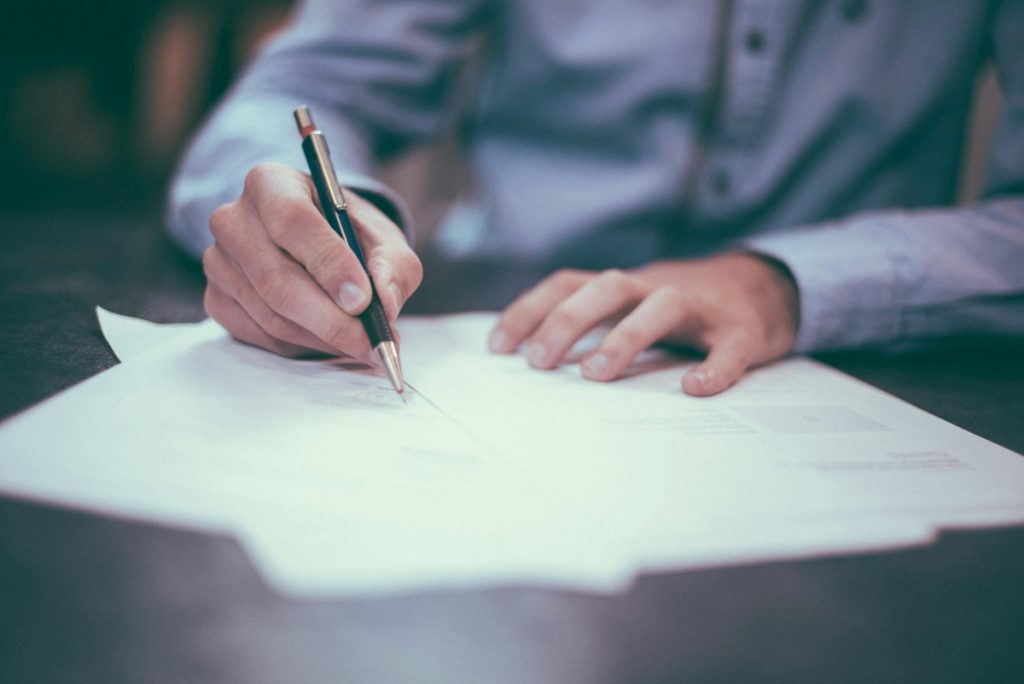 Hand holding a pen while signing a document at a desk