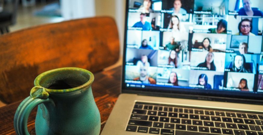 Laptop on a table showing a video call grid of colleagues, with a coffee mug beside it