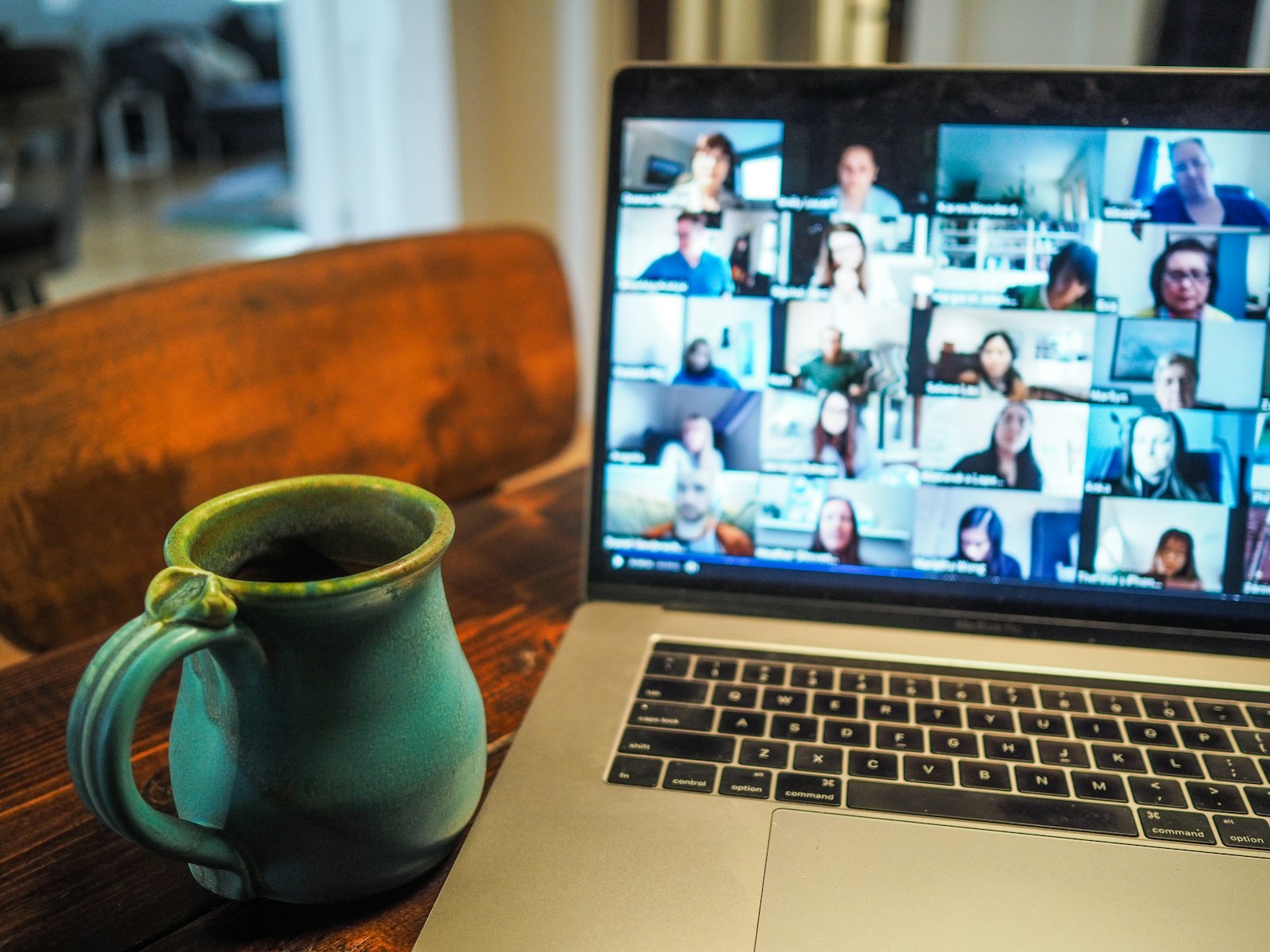 Laptop on a table showing a video call grid of colleagues, with a coffee mug beside it