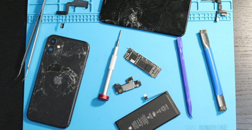 A disassembled iPhone and repair tools laid out on a blue repair mat