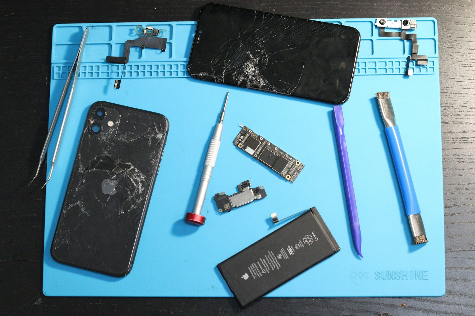 A disassembled iPhone and repair tools laid out on a blue repair mat
