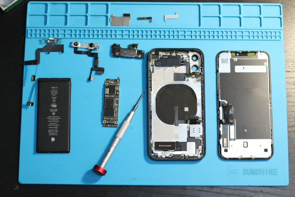 iPhone components, including the screen and internal parts, disassembled and arranged on a blue mat