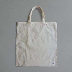 Plain white reusable cotton tote bag lying on a grey surface