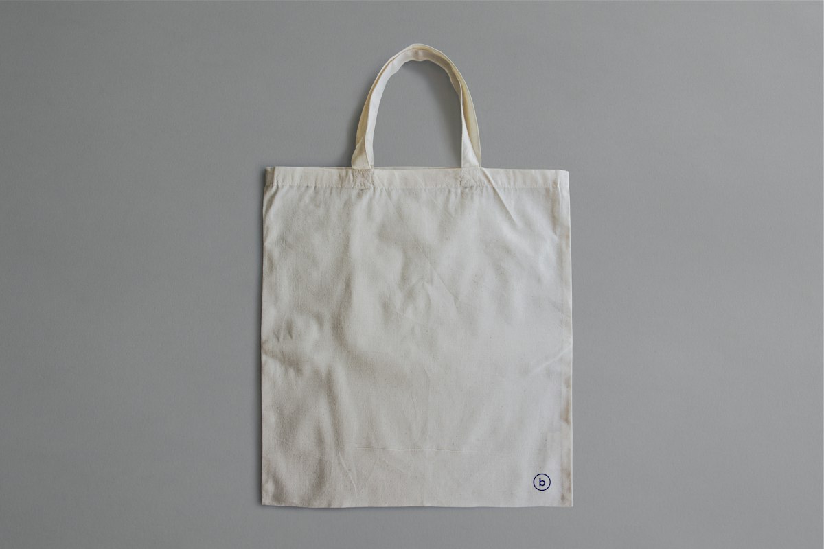 Plain white reusable cotton tote bag lying on a grey surface