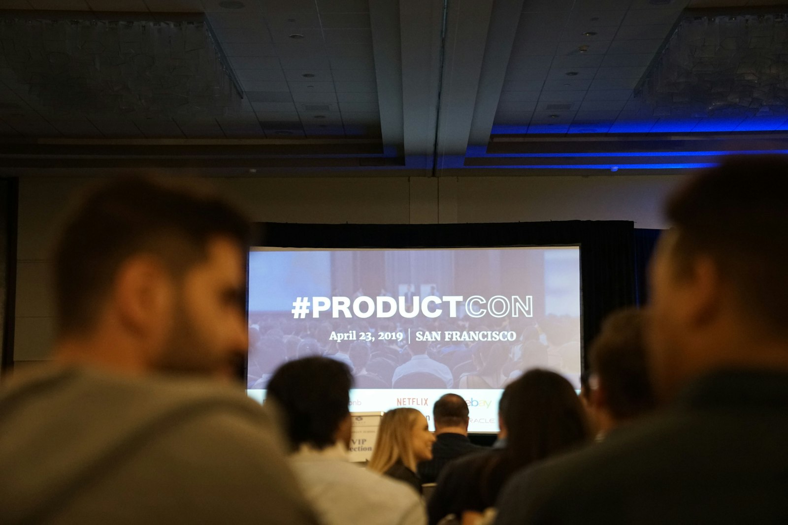 Audience seated in a conference hall facing a large projector screen during a presentation