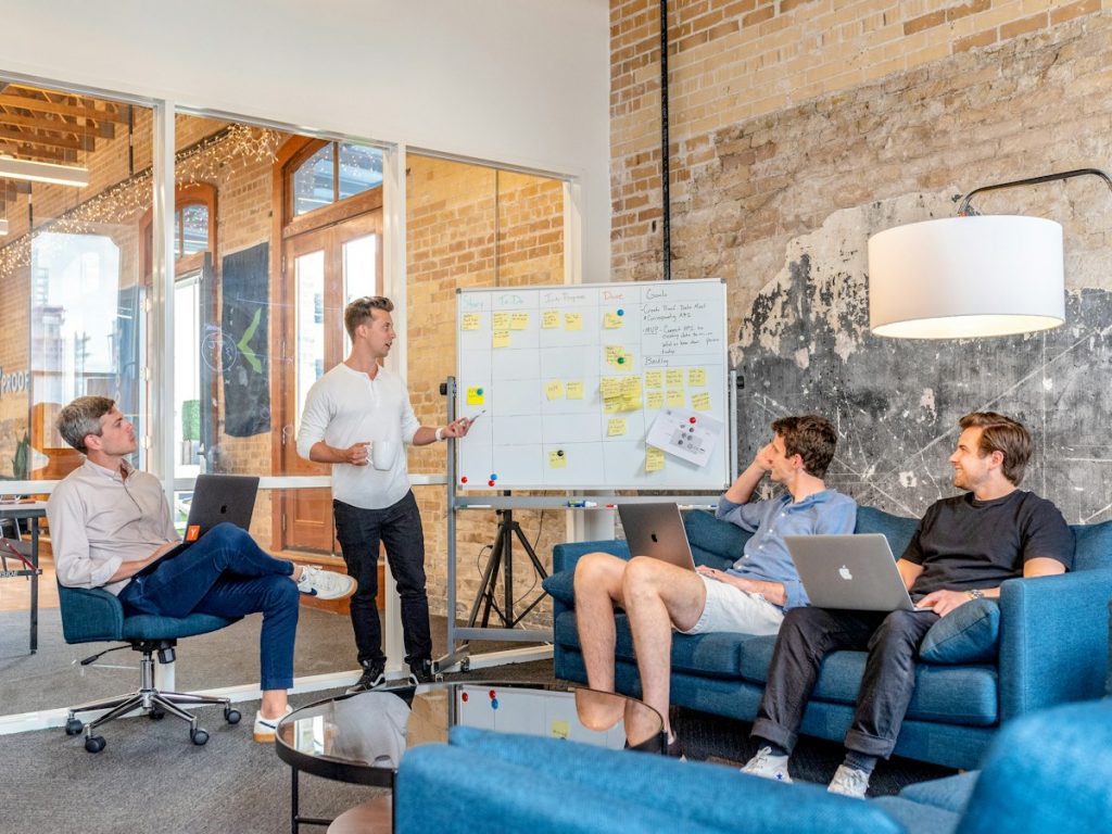 Three people with laptops watching a presenter at a whiteboard in an office meeting room