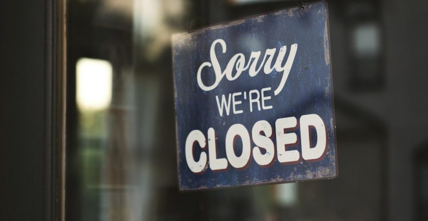 A 'Sorry we're closed' sign hanging on a glass shop door